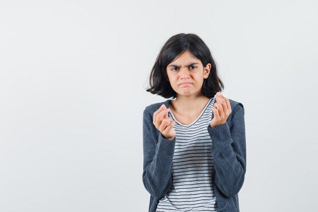 Little girl doing money gesture in t-shirt, jacket and looking indigent.