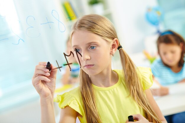 Little girl doing sum with classmates on background