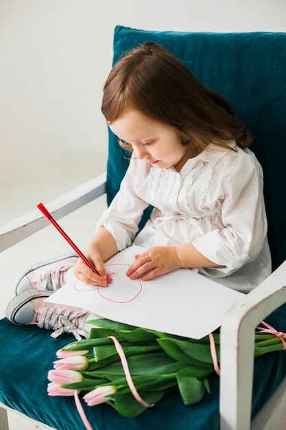 Little girl drawing heart on paper sheet