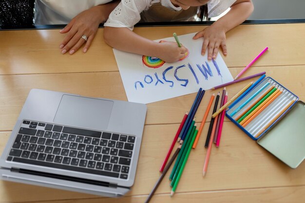 Little girl drawing an i miss you message on paper for a video call