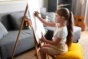 Бесплатное фото Маленькая девочка рисует с помощью мольберта