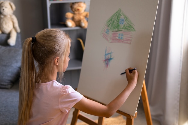 Маленькая девочка рисует с помощью мольберта