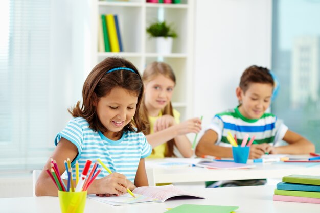 Little girl drawing with classmates on background