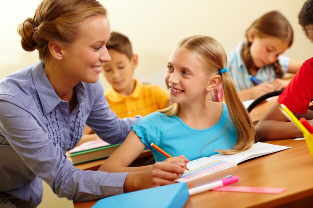 Little girl drawing with teacher helping in class