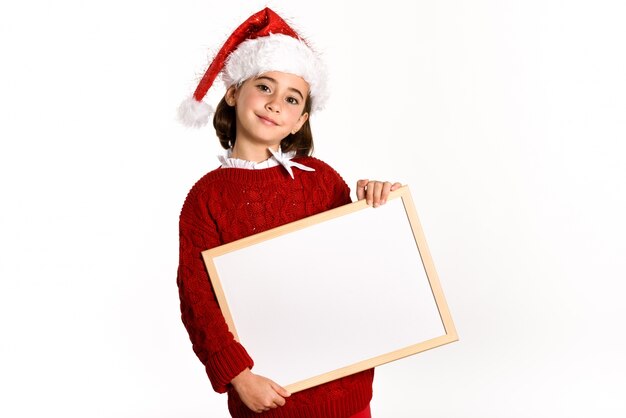 Little girl dressed as santa claus holding a white board in a white background