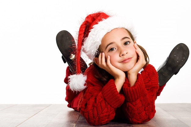 Little girl dressed as santa claus lying on the floor with hands on face