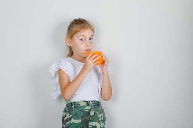 Маленькая девочка пьет фруктовый сок в белой футболке