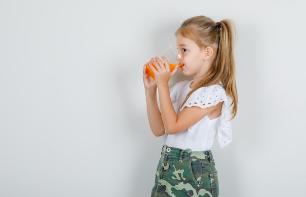 Bambina che beve succo e distoglie lo sguardo in maglietta bianca