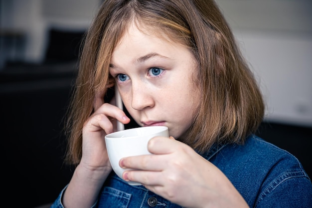 Little girl drinks tea and looks surprised talking on the phone