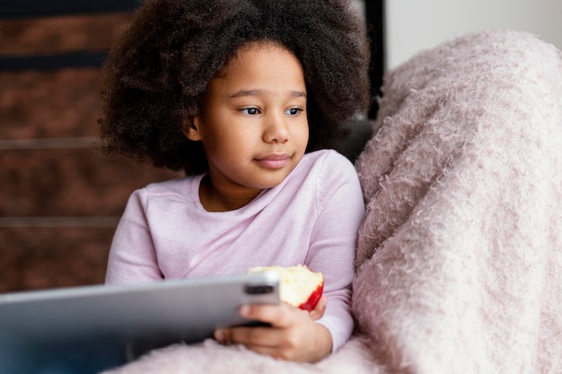 Free photo little girl eating apple and using tablet