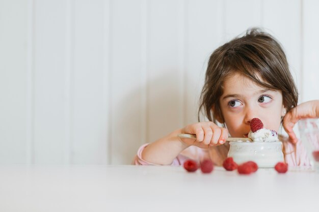 Little girl eating fresh raspberry with cream