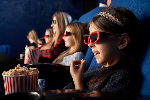 Little girl eating popcorn, watching cartoon in cinema.