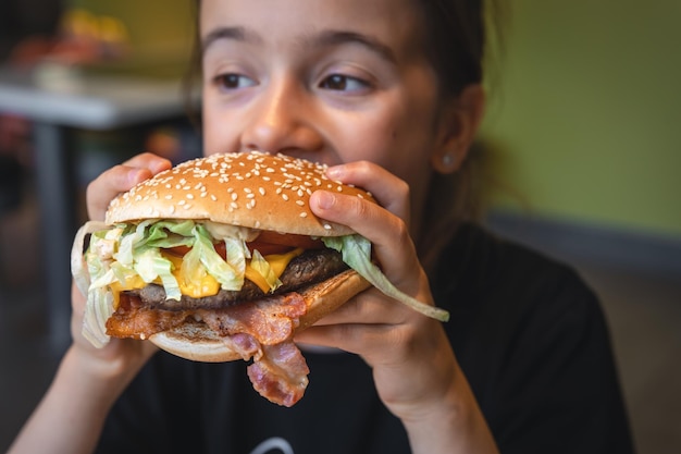 어린 소녀는 식욕을 돋우는 햄버거 근접 촬영을 먹는다