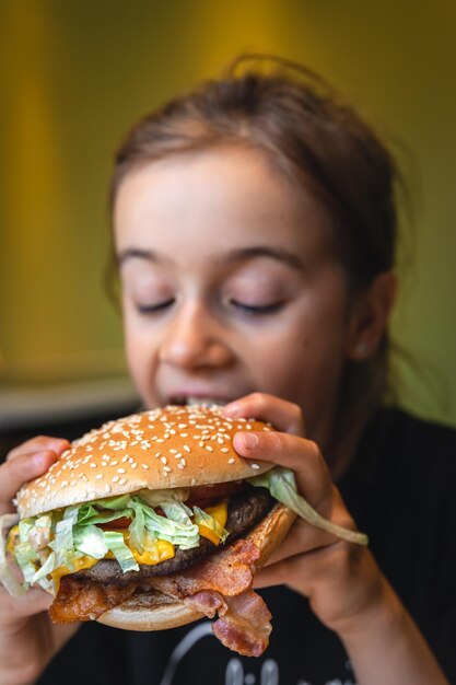 小さな女の子が食欲をそそるハンバーガーのクローズ アップを食べる
