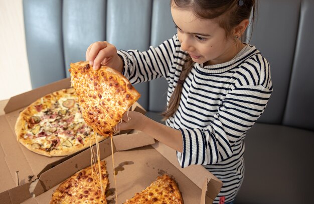 Маленькая девочка ест аппетитную сырную пиццу на обед.
