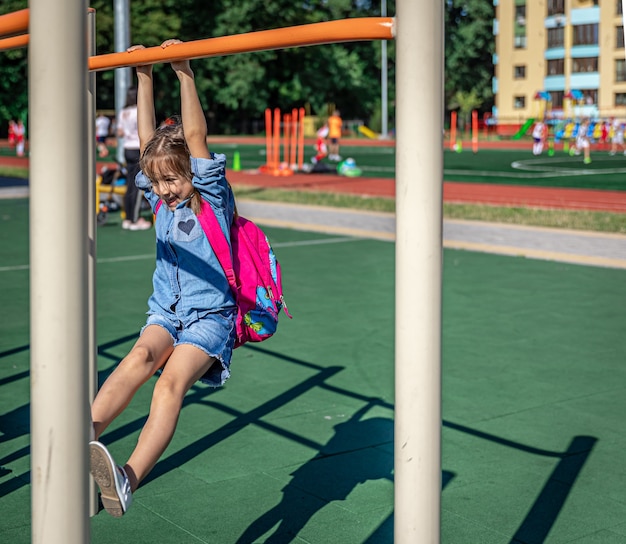 A little girl, an elementary school student, plays on the playground after school, pulls herself up on a horizontal bar.