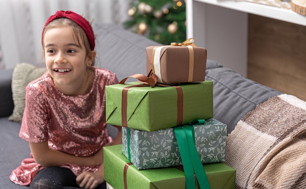 小さな女の子は家のソファに座ってたくさんのクリスマスプレゼントを楽しんでいます