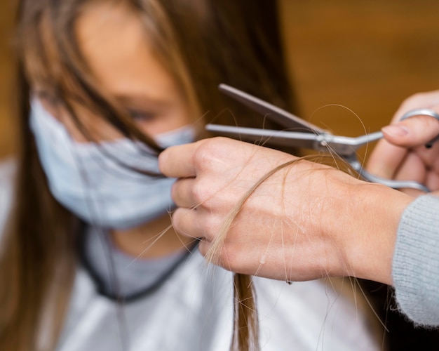 Little girl getting a haircut while wearing medical mask