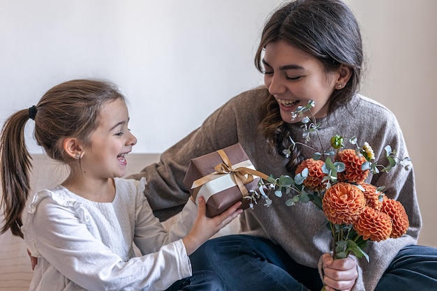 Маленькая девочка дарит маме подарочную коробку и букет цветов хризантемы, концепцию дня матери, дня рождения, женского дня.