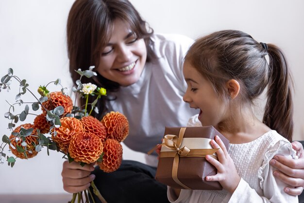 A little girl gives her mother a gift and a bouquet of flowers