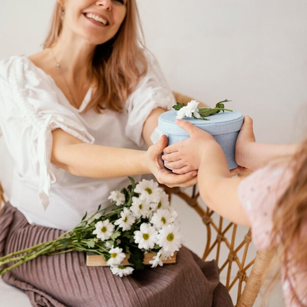 Little girl giving spring flowers and gift box to mom
