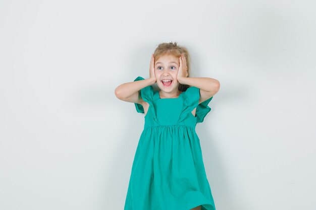 Little girl in green dress holding head with hands and looking happy