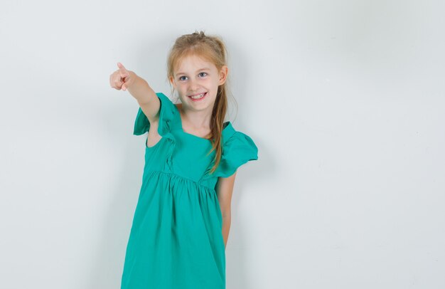 Little girl in green dress pointing finger away and looking cheerful