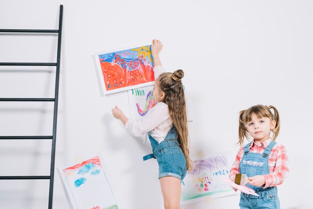 Little girl hanging drawings on wall