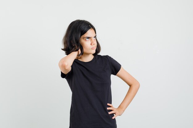 어린 소녀는 검은 색 티셔츠에 목에 통증이 있고 불편한 전면보기를보고 있습니다.