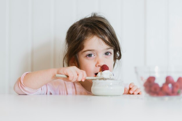 Little girl having raspberry with cream