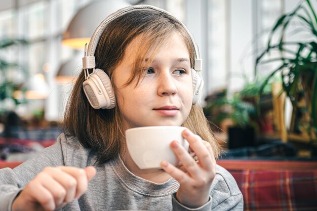 A little girl in headphones in a cafe with a cup of tea