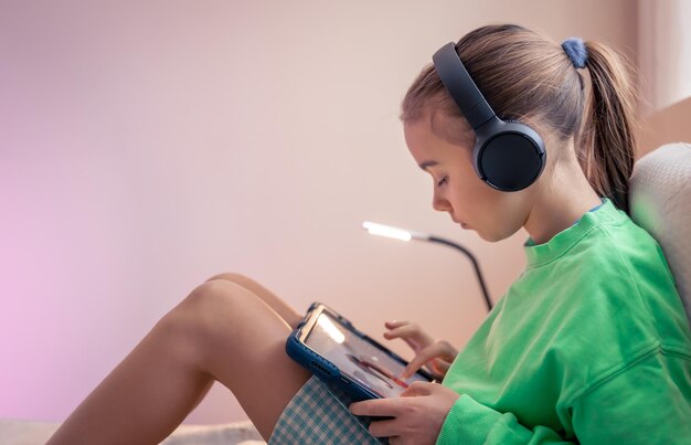 little girl in headphones with a tablet in her room