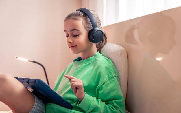 little girl in headphones with a tablet in her room