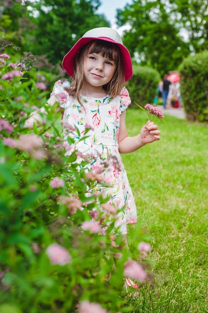Little girl behind a hedge with flowers in a hand