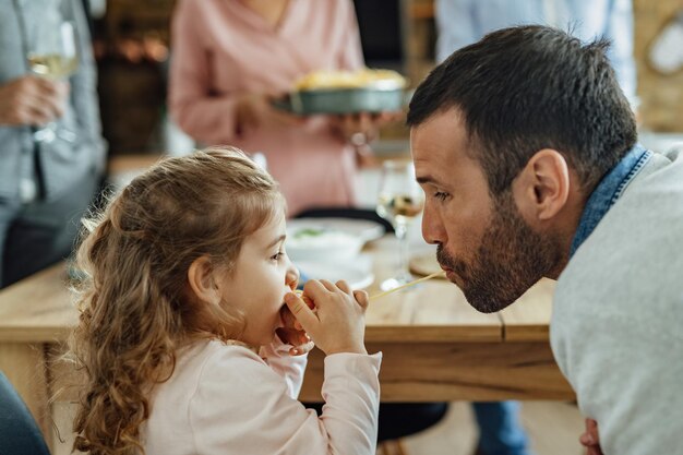 Little girl and her father sharing a spaghetti while eating at dining table