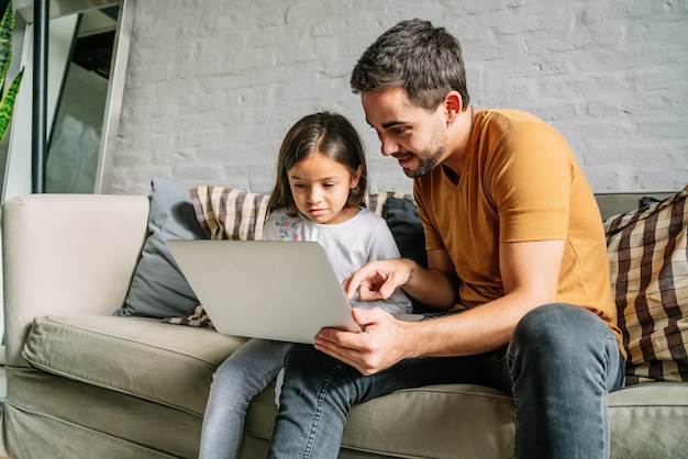 어린 소녀와 그녀의 아버지는 집에서 함께 노트북을 사용합니다.