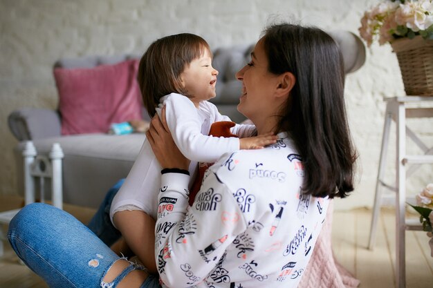 カジュアルなスタイルに身を包んだ小さな女の子と彼女のお母さんは床で遊んで楽しんで