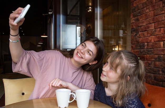 A little girl and her older sister are taking a selfie in a cafe