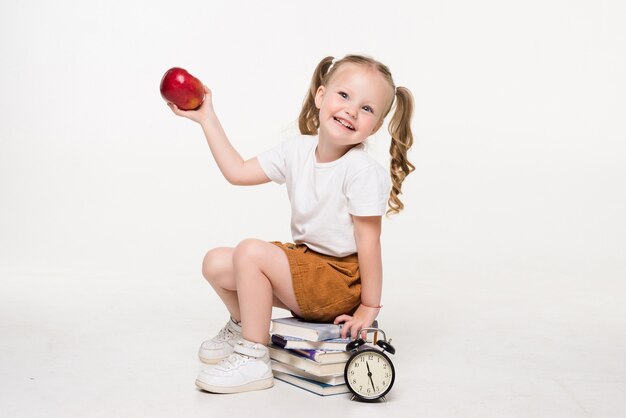 Bambina che tiene mela seduta su una pila di libri isolati