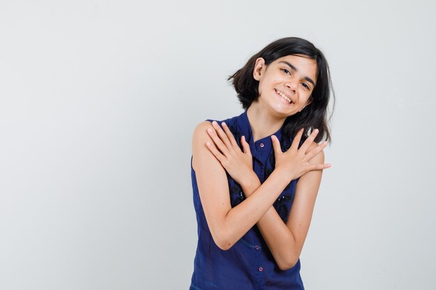 Little girl holding arms crossed in blue blouse and looking merry. front view.