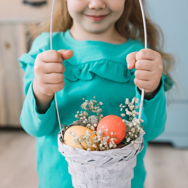 Маленькая девочка держит корзину с пасхальными яйцами