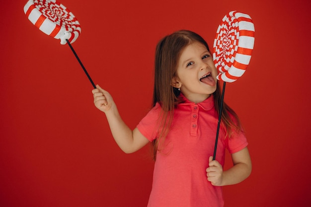 Little girl holding big lollypop isolated on red background