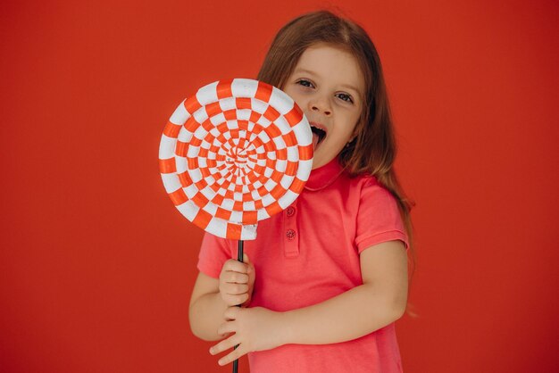 Little girl holding big lollypop isolated on red background