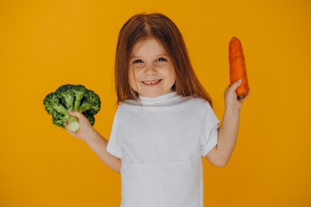Маленькая девочка держит брокколи и морковь