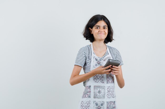 Tシャツ、エプロン、陽気に見える電卓を持っている少女。