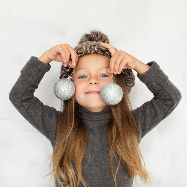 Little girl holding christmas globes close to her face