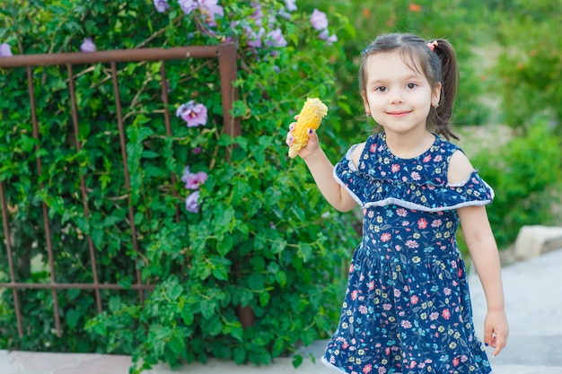Little girl holding corn and looking at camera in garden in spring dress and looking happy. front view.