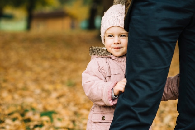 Little girl holding on dad's legs in autumn park