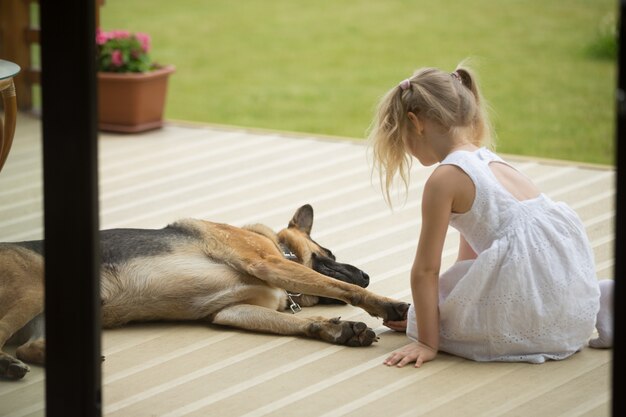 Маленькая девочка держит собачью лапу возле домашнего животного на крыльце