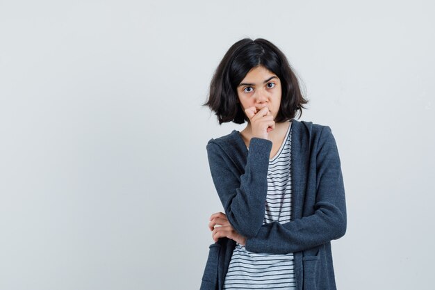 Little girl holding hand on chin in t-shirt, jacket and looking thoughtful ,